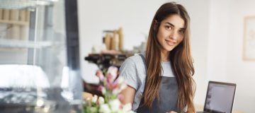 Coffee shop owner using a tablet looking at camera smiling, waiting for her first customer